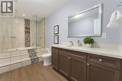 Bathroom featuring a built-in tub and shower combination with clear glass enclosure, a mosaic tile accent wall, wood-finish flooring, a vanity with a light-colored countertop, and a large framed mirro - 
