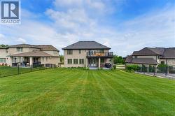 Expansive backyard featuring a manicured lawn, a two-story brick exterior, a second-story balcony with dark railings, a ground-level covered patio, and a dark metal fence - 