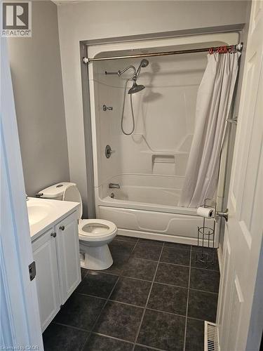 Bathroom featuring a white integrated shower/tub unit, dark square floor tiles, a white vanity with a single basin, and a toilet - 19 Glenayr Street, Hamilton, ON 
