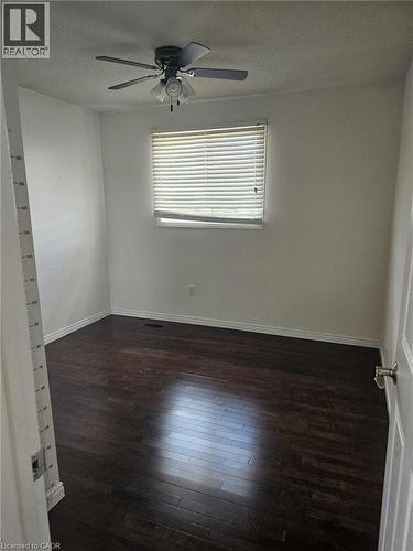 Interior room featuring dark wood-finish flooring, white wall paint, and a window with horizontal blinds - 19 Glenayr Street, Hamilton, ON 