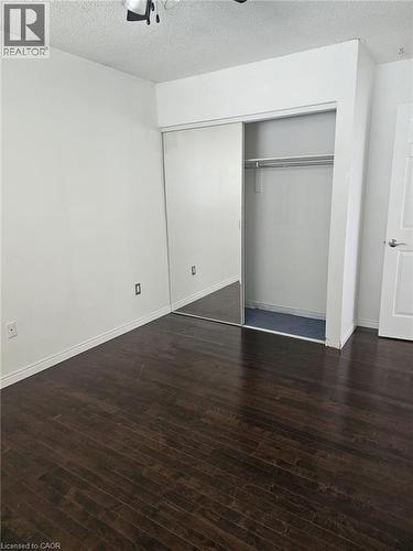 Room featuring dark wood-finish flooring, white baseboards, and a wardrobe with sliding doors - 19 Glenayr Street, Hamilton, ON 