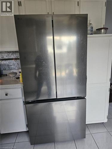 Stainless steel French door refrigerator with a bottom freezer drawer, white cabinetry with silver hardware, light-colored countertops, and a subway tile backsplash - 19 Glenayr Street, Hamilton, ON 