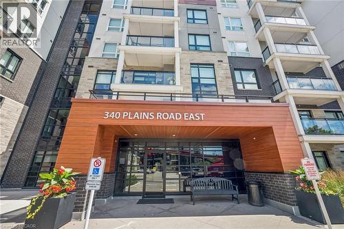 Modern building exterior featuring a wood-finish entrance canopy, dark brick accents, and stone facade - 340 Plains Road E Unit# 507, Burlington, ON - Outdoor With Balcony
