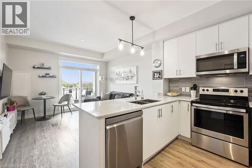 Open-concept living space featuring a modern kitchen with white cabinetry, stainless steel appliances, and light-toned countertops - 340 Plains Road E Unit# 507, Burlington, ON - Indoor Photo Showing Kitchen With Stainless Steel Kitchen With Double Sink