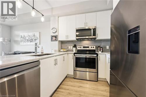 Well-appointed kitchen featuring white cabinetry, stainless steel appliances, a grey tiled backsplash, wood-finish flooring, and track lighting - 340 Plains Road E Unit# 507, Burlington, ON - Indoor Photo Showing Kitchen With Stainless Steel Kitchen With Double Sink