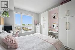 Bedroom featuring a large window, light gray wall color, built-in white cabinetry with gold-tone hardware, and an integrated vanity area - 