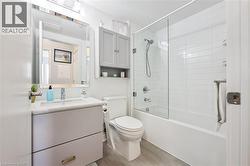 Contemporary bathroom featuring a grey vanity with a white countertop and undermount sink, a framed mirror, a wall-mounted medicine cabinet, a toilet, and a combined bathtub and shower with a glass en - 