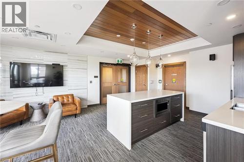 Open-concept living area featuring a central island with integrated microwave, pendant lighting, and wood-panel ceiling accents - 340 Plains Road E Unit# 507, Burlington, ON - Indoor