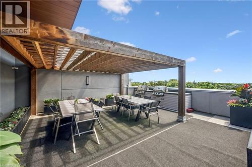 Expansive outdoor deck featuring a large wooden pergola, built-in outdoor kitchen with grills, integrated planters, and a textured dark gray surface - 340 Plains Road E Unit# 507, Burlington, ON - Outdoor With Exterior