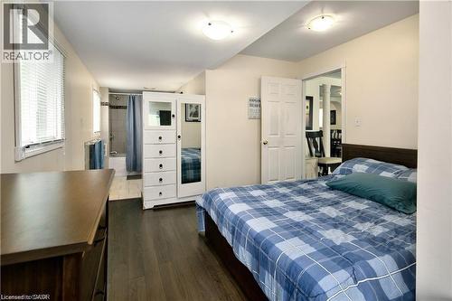 Bedroom featuring wood-finish flooring, an adjacent three-piece bathroom with a tiled shower, and a pair of windows with blinds - 42 5Th Lane, Wasaga Beach, ON - Indoor Photo Showing Bedroom