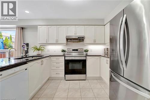 Kitchen featuring white cabinetry, dark countertops, stainless steel appliances, and tile flooring - 35 Dubrick Crescent, Kitchener, ON 