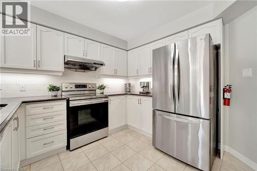 Kitchen featuring white cabinetry, dark countertops, a stainless steel electric range, an overhead stainless steel range hood, and a stainless steel French door refrigerator - 35 Dubrick Crescent, Kitchener, ON 