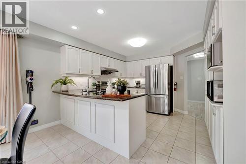 Bright kitchen featuring an island with a dark countertop and white cabinetry - 35 Dubrick Crescent, Kitchener, ON 