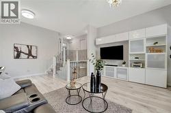 Living area featuring light wood-finish flooring, a contemporary built-in media center with integrated shelving, a staircase with dark metal spindles and a white handrail, and modern flush-mount ceili - 