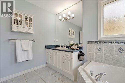 Bathroom featuring a built-in corner tub, white vanity with integrated sink, full-width wall mirror, and privacy window - 35 Dubrick Crescent, Kitchener, ON 