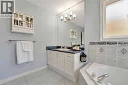 Bathroom featuring a built-in corner tub, white vanity with integrated sink, full-width wall mirror, and privacy window - 