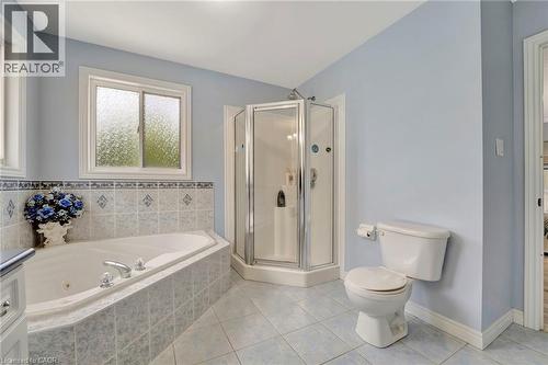 Bathroom featuring a corner soaking tub with tiled surround, a glass-enclosed shower, and a white toilet - 35 Dubrick Crescent, Kitchener, ON 