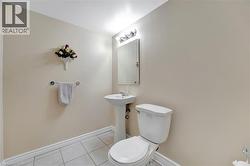 Bathroom featuring neutral wall paint, white tiled flooring, a pedestal sink, and a toilet - 