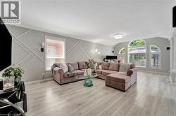 Spacious living area featuring light wood-finish flooring, accent wall paneling, and an array of large arched windows - 
