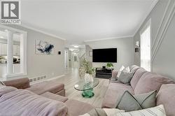 Spacious living area featuring light wood-finish flooring, crown molding, and a decorative accent wall - 