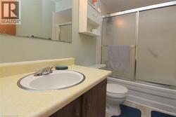 Bathroom featuring a white drop-in sink, chrome faucet, and a shower-tub combination with sliding frosted glass doors - 