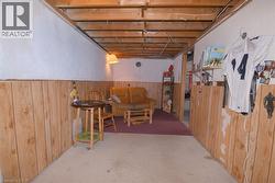 Finished basement area featuring exposed ceiling joists, wood-finish wall paneling, and concrete flooring - 