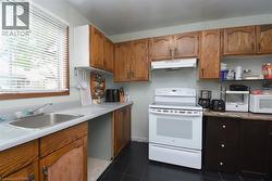Kitchen featuring a stainless steel sink, wood-finish cabinetry, a white electric range with overhead ventilation, and dark tile flooring - 