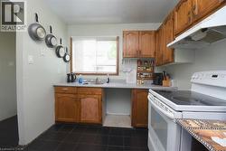 Kitchen featuring dark tile flooring, wood cabinetry, a window with blinds, a stainless steel sink, and a white oven with a stovetop - 