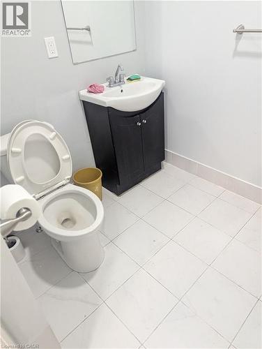 Bathroom featuring a white toilet, black vanity with a white basin sink, and a wall-mounted mirror - 499 Main Street E, Hamilton, ON 