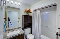 Bathroom featuring a white bathtub with a shower kit, a dark wood-finish vanity with a granite-style countertop, a rectangular undermount sink, and a mirrored wall cabinet with integrated vanity light - 