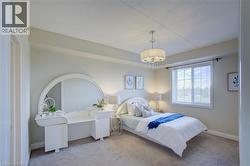 Soft neutral wall tones featuring a large window with horizontal blinds, a ceiling-mounted chandelier, and carpet flooring - 