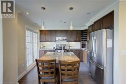 Chef's kitchen featuring an expansive center island with seating, stainless steel appliances, dark wood cabinetry, crown molding, and sliding glass doors - 