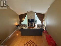 Spacious living area featuring a vaulted ceiling with crown molding, a stone-clad fireplace, and wood-finish flooring with a decorative inlay - 