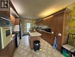 Kitchen featuring wood-finish cabinetry, a central island with an integrated sink, a built-in double oven, and a gas range - 