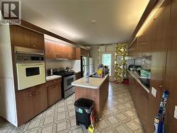 Galley kitchen featuring wood-finish cabinetry, a built-in oven, and a central island with an integrated sink - 