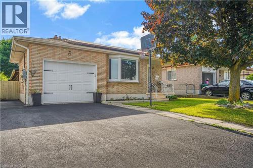 Brick facade residence featuring an attached garage with a decorative door, a paved driveway, and a front lawn with a mature tree - 234 Thunderbird Drive, Cambridge, ON - Outdoor