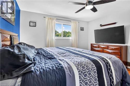 Spacious bedroom featuring light gray walls with a contrasting blue accent wall, a ceiling fan, a window with exterior tree views, and wood-finish flooring - 234 Thunderbird Drive, Cambridge, ON - Indoor Photo Showing Bedroom