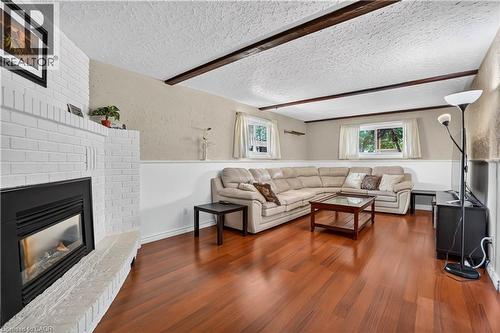Living space featuring a white brick fireplace with a black insert, wood-finish flooring, exposed ceiling beams, and multiple windows - 234 Thunderbird Drive, Cambridge, ON - Indoor Photo Showing Living Room With Fireplace