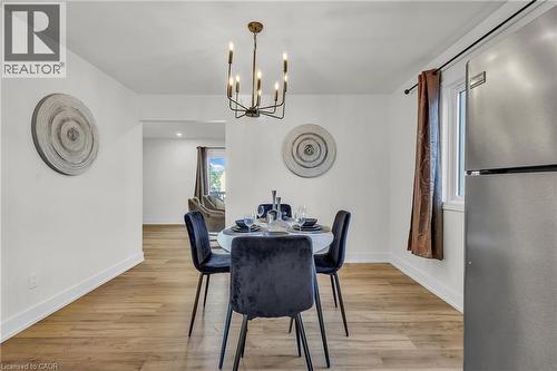 Dining area featuring wood-finish flooring, a contemporary chandelier, and an open layout to an additional living space - 127 Acorn Crescent, London, ON 