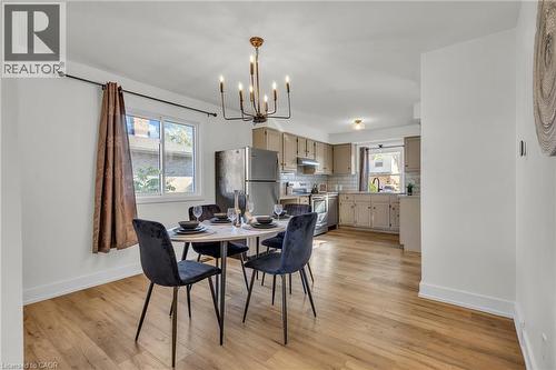 Open-concept living space featuring wood-finish flooring, a modern chandelier, and a kitchen with light-toned cabinetry, subway tile backsplash, and stainless steel appliances - 127 Acorn Crescent, London, ON 
