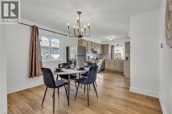 Open-concept living space featuring wood-finish flooring, a modern chandelier, and a kitchen with light-toned cabinetry, subway tile backsplash, and stainless steel appliances - 