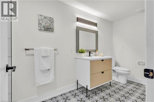 Bathroom featuring patterned floor tiling, a modern vanity with wood-finish drawer fronts, a rectangular mirror with a gray frame, and a wall-mounted light fixture - 127 Acorn Crescent, London, ON 