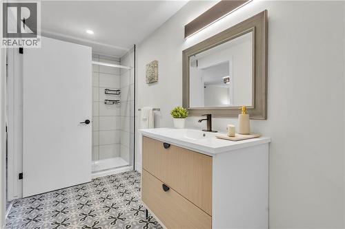 Bathroom featuring a wood-finish vanity with a white countertop and integrated sink, framed mirror with integrated lighting, and patterned floor tiling - 127 Acorn Crescent, London, ON 