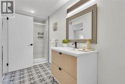Bathroom featuring a wood-finish vanity with a white countertop and integrated sink, framed mirror with integrated lighting, and patterned floor tiling - 