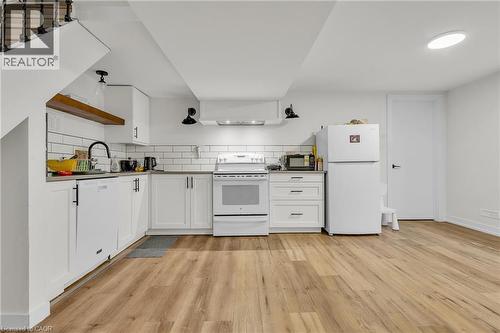 Kitchen featuring white cabinetry, subway tile backsplash, wood-finish flooring, a stainless steel sink with a matte black faucet, and a large white refrigerator - 127 Acorn Crescent, London, ON 