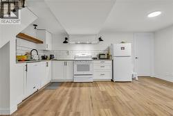 Kitchen featuring white cabinetry, subway tile backsplash, wood-finish flooring, a stainless steel sink with a matte black faucet, and a large white refrigerator - 