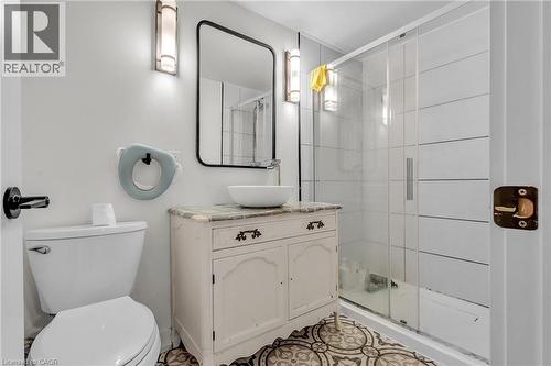 Bathroom featuring patterned floor tiles, a glass-enclosed shower with horizontal white wall tiles, and a white vanity with a vessel sink - 127 Acorn Crescent, London, ON 