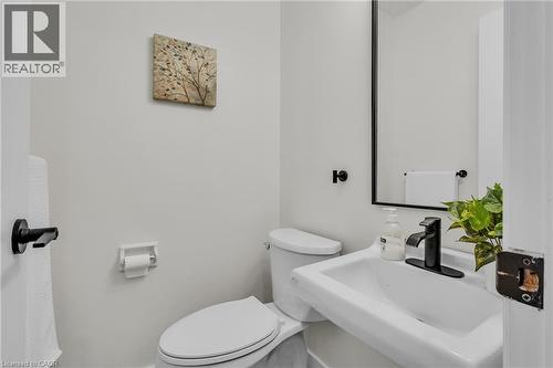 Modern powder room featuring a wall-mounted sink, matte black faucet, and rectangular mirror - 127 Acorn Crescent, London, ON 