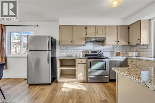 Kitchen featuring light wood-finish flooring, white subway tile backsplash, stainless steel appliances, speckled stone countertops, and beige cabinetry - 127 Acorn Crescent, London, ON 