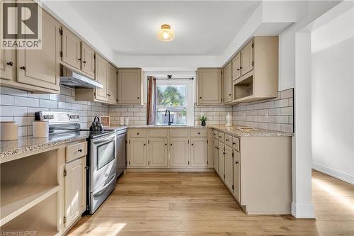 U-shaped kitchen featuring wood-finish flooring, white subway tile backsplash, and light-toned cabinetry with dark hardware - 127 Acorn Crescent, London, ON 